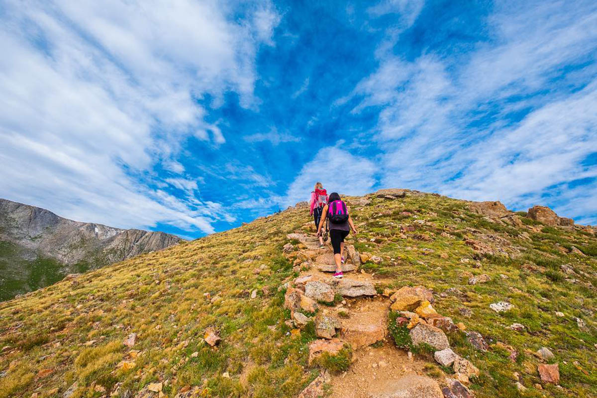 Hikers wearing backpacks reaching the summit of a hike.